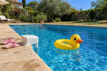 Une alarme de piscine blanche vissée sur la margelle, une bouée canard qui flotte à côté