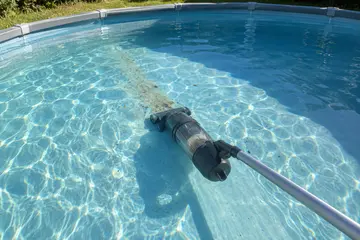 Un aspirateur à batterie au fond d'une petite hors sol, du sable fin devant sa tête