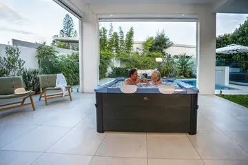 Un couple dans un MSpa Oslo teinte Sapphire, sous une pergola au bord d'une piscine