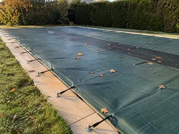 Une bâche d'hivernage vert foncé tendue sur une enterrée, les sandows accrochés à la margelle