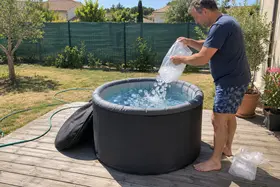 Un homme verse un sac de glaçons dans un bain froid gonflable, en plein soleil