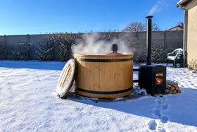 Un bain nordique en bois fume dans la neige, le poêle allumé à côté, quelqu'un dedans
