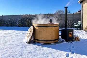 Un bain nordique en bois fume dans la neige, le poêle allumé à côté, quelqu'un dedans