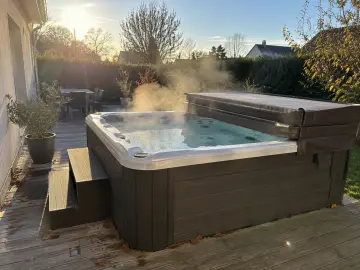 Un spa rigide sur une terrasse bois, sa couverture repliée, l'eau qui fume au froid