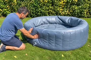 Un homme à genoux presse la paroi affaissée d'un spa gonflable à moitié dégonflé