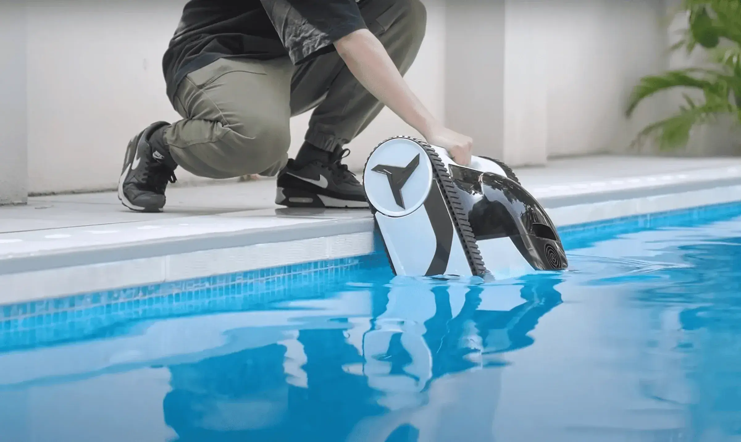 Un robot noir et blanc bascule dans l'eau claire, tenu par une main au bord du bassin