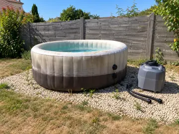 Un spa gonflable délavé par le soleil, son bloc technique débranché posé à côté sur le gravier