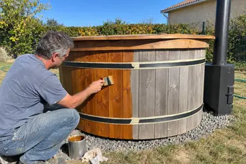 Un propriétaire huile au pinceau la paroi en bois de son bain nordique