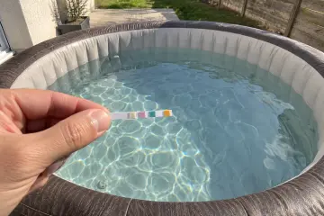Une bandelette de test tenue entre deux doigts au-dessus de l'eau du spa