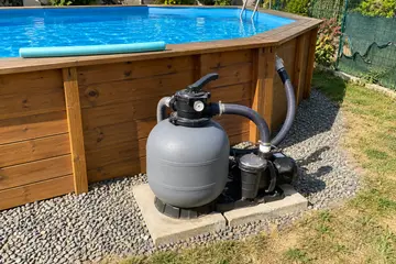 Un filtre à sable et sa vanne au pied d'une piscine hors sol en bois