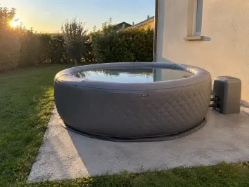 Un spa gonflable sur sa dalle béton, le tapis gris dessous, la pelouse autour