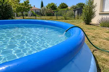 Une piscine autoportante ronde au boudin gonflé, remplie au tuyau sur une pelouse sèche