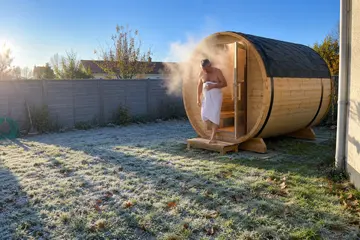 Un homme en serviette sort du sauna tonneau, la vapeur dans le froid du matin