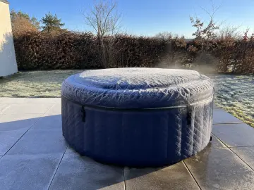 Spa gonflable sous son couvercle givré, un filet de vapeur au bord, terrasse gelée