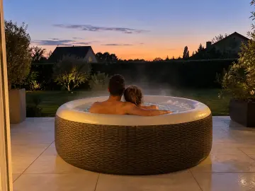 Un couple de dos dans un spa gonflable rond qui fume, le soir