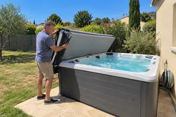 Un propriétaire replie la couverture isolante de son spa rigide en plein soleil