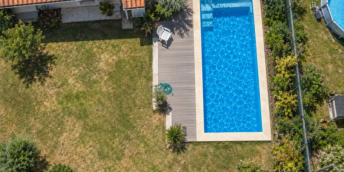 Une piscine enterrée vue du ciel, au milieu d'un jardin de lotissement