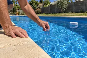 Une main remplit une trousse d'analyse dans la piscine, un analyseur flotte derrière